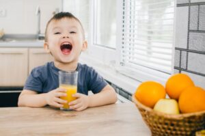 Happy little boy holding a glass of orange juice